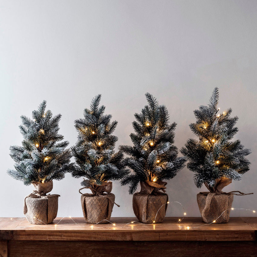 Four pre lit mini Christmas trees on a sideboard
